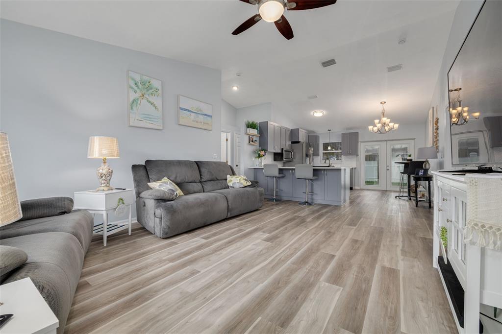 An open-concept living room and kitchen featuring gray cabinetry, light wood-look flooring, and a ceiling fan — 1848 77TH AVENUE N, ST PETERSBURG, FL