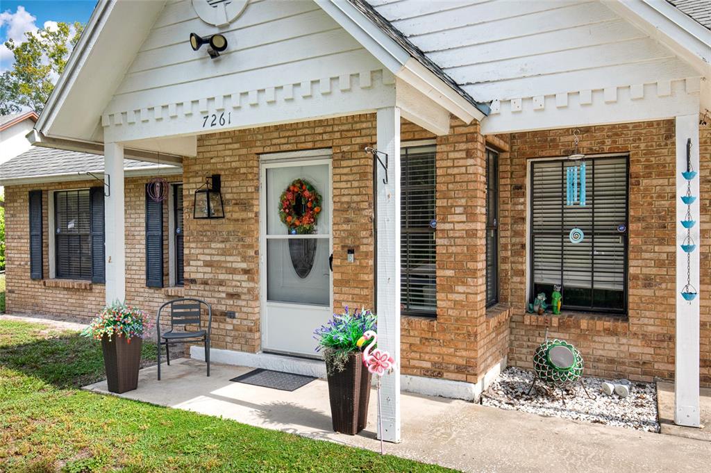 A brick house exterior features a covered front porch with a white door and shutters — 7261 ABBEY LANE, WINTER PARK, FL