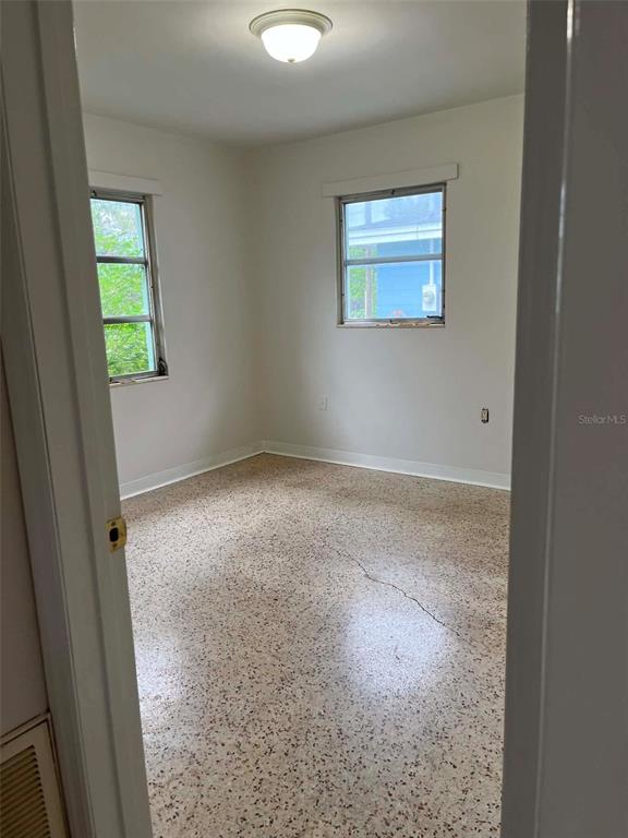 An empty bedroom features light-colored walls, two windows, and a speckled terrazzo floor — 6445 RIVER ROAD, NEW PORT RICHEY, FL