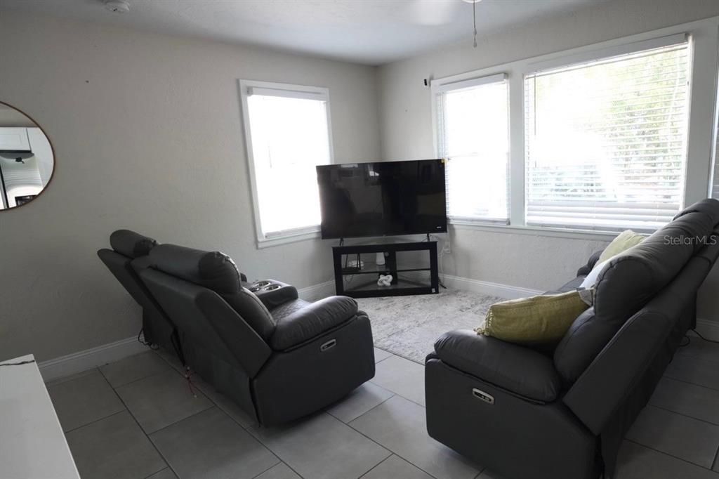 A living room features two gray reclining sofas, a television on a stand, and tile flooring — 4405 N TAMPANIA AVENUE, TAMPA, FL