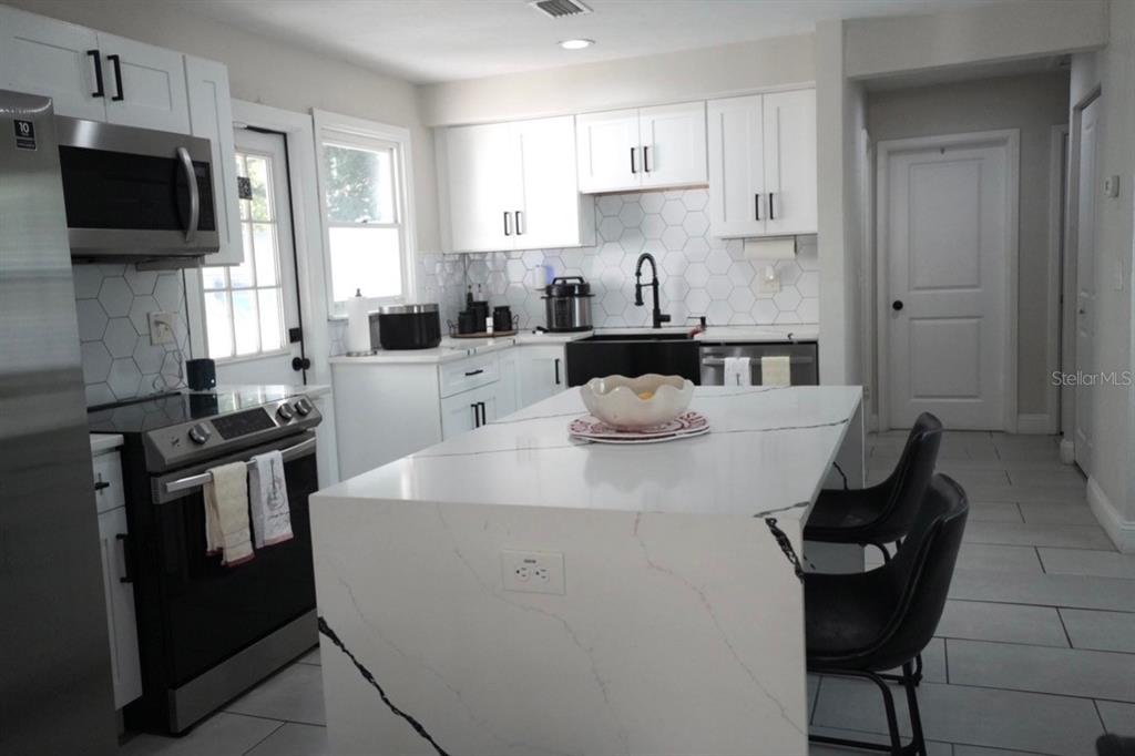 A modern kitchen features white cabinetry, a marble-topped island, and a hexagonal tile backsplash — 4405 N TAMPANIA AVENUE, TAMPA, FL