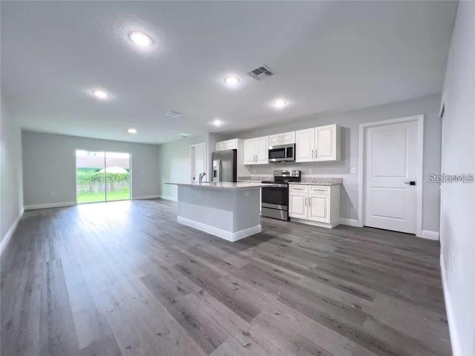 An open-concept kitchen and living area features white cabinetry, stainless steel appliances, and wood-look flooring — 13435 KAPLAN TERRACE, PORT CHARLOTTE, FL