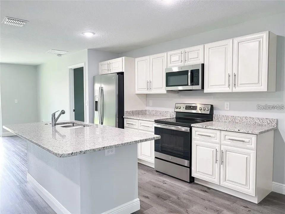 A kitchen features white cabinets, granite countertops, stainless steel appliances, and a central island — 13435 KAPLAN TERRACE, PORT CHARLOTTE, FL