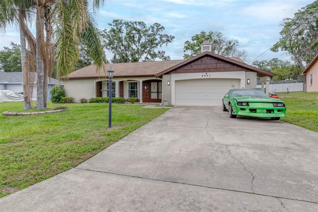A single-story brick house with a brown shingled roof and a bright green car parked outside — 8441 BRAGANZA STREET, SPRING HILL, FL