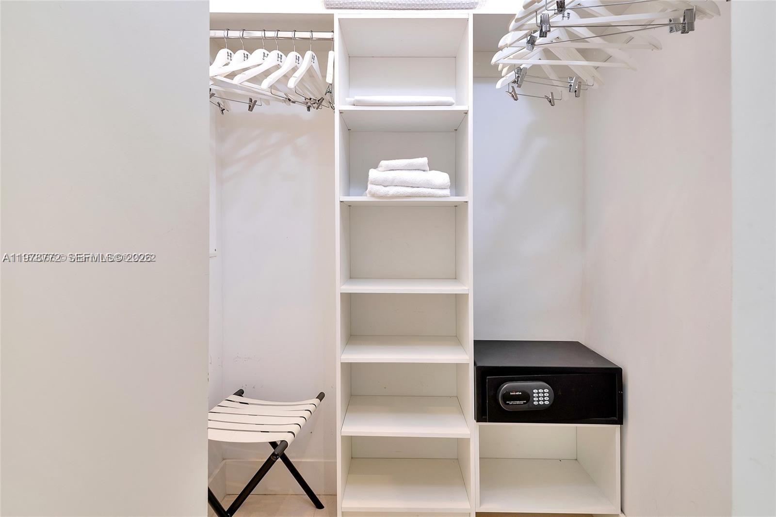 A walk-in closet features white shelving, hanging rods with hangers, a small safe, and a stool — 4111 S Ocean Dr # 302, Hollywood FL 33019, HOLLYWOOD, FL