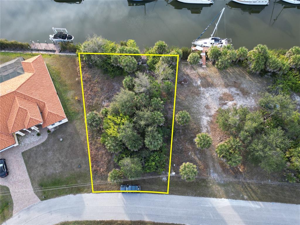 An aerial view shows a vacant, wooded waterfront lot outlined in yellow along a road — 10481 REDONDO STREET, PORT CHARLOTTE, FL