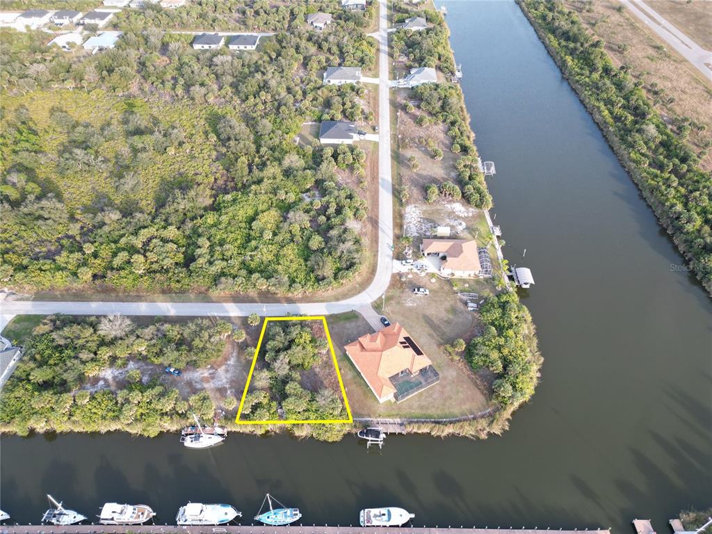 An aerial view shows a vacant, wooded waterfront lot outlined in yellow next to a house — 10481 REDONDO STREET, PORT CHARLOTTE, FL