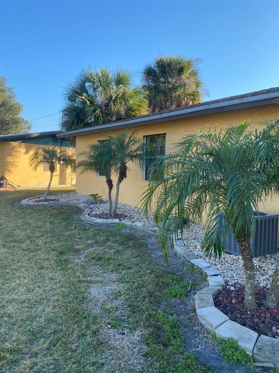 A yellow house exterior features palm trees and stone-bordered landscaping beds in the yard — 1587 WAYMAN ROAD, MOORE HAVEN, FL