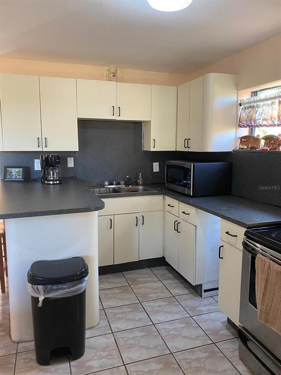 A kitchen features white cabinets, dark countertops, a microwave, and tiled flooring — 1587 WAYMAN ROAD, MOORE HAVEN, FL