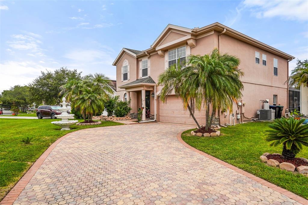 A two-story tan stucco house with a paved driveway, palm trees, and a front fountain — 12341 ACCIPITER DRIVE, ORLANDO, FL