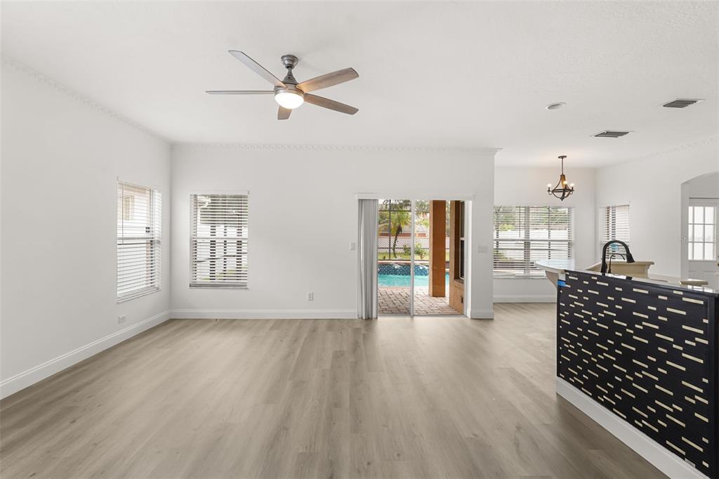 An open-concept living area with light wood-look flooring, a ceiling fan, and sliding glass doors — 12341 ACCIPITER DRIVE, ORLANDO, FL