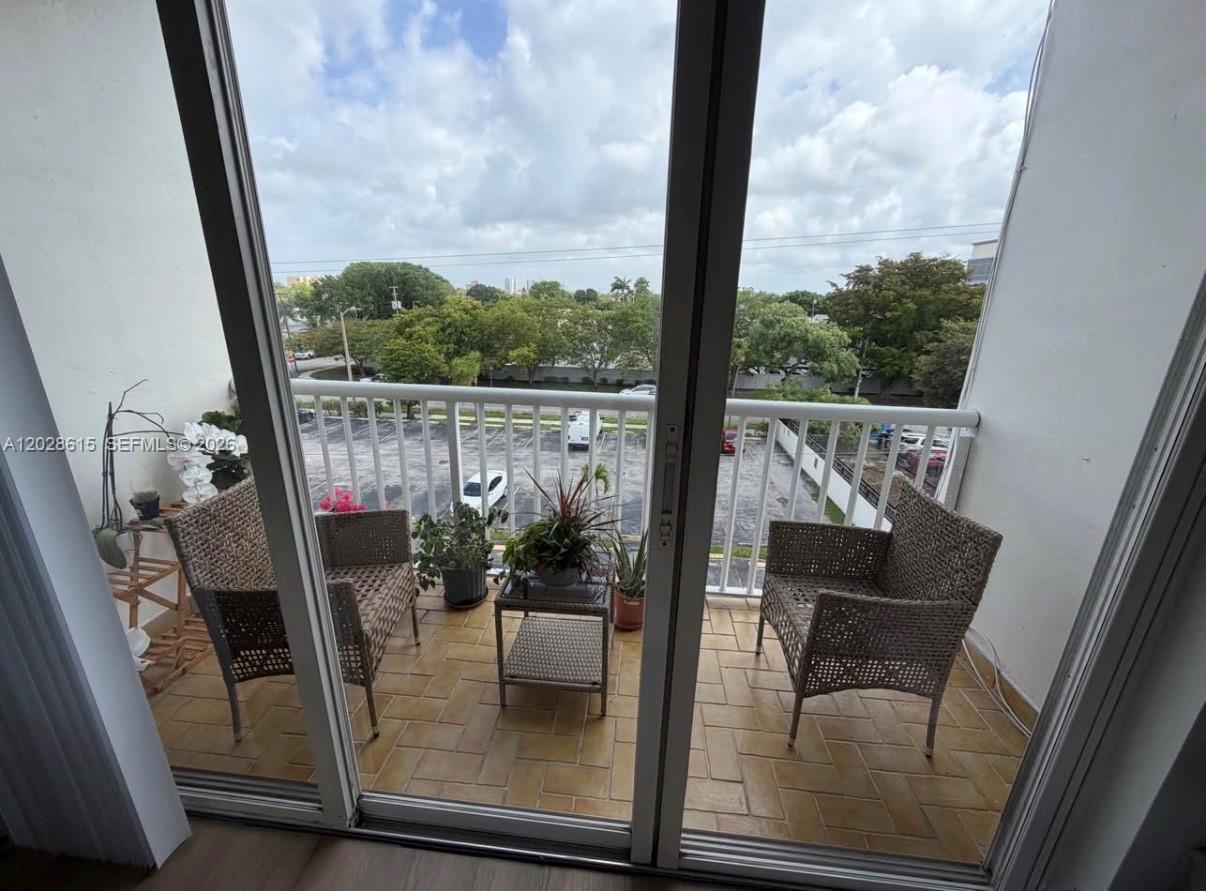 A balcony with two wicker chairs, a small table, and potted plants overlooks a parking lot — 3551 SW 9th Ter # 409, Miami FL 33135, MIAMI, FL