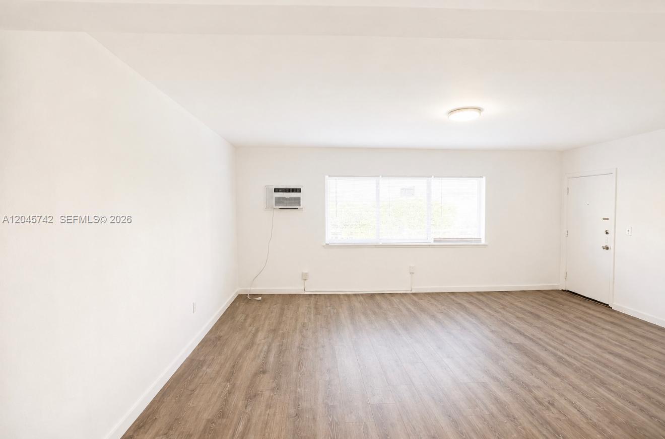 An empty room features white walls, wood-look flooring, a window, and a wall-mounted air conditioner — 7600 Dickens Ave # 2, Miami Beach FL 33141, MIAMI BEACH, FL