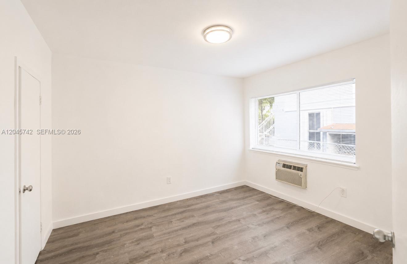 An empty bedroom features white walls, wood-look flooring, a window, and a wall-mounted air conditioner — 7600 Dickens Ave # 2, Miami Beach FL 33141, MIAMI BEACH, FL