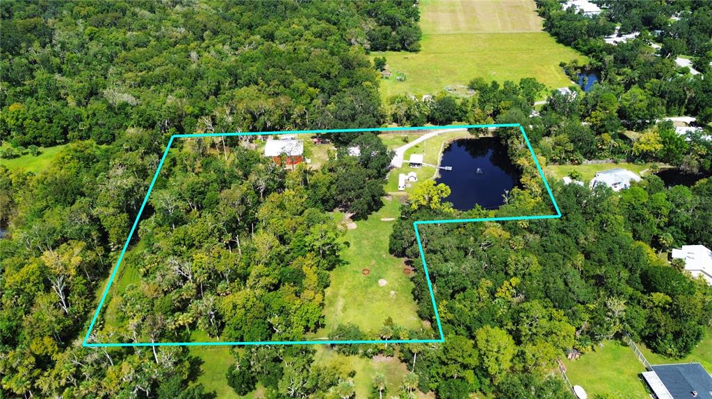 An aerial view shows a rural property with a house, pond, and surrounding wooded acreage — 2310 DOSTER DRIVE, NEW SMYRNA BEACH, FL