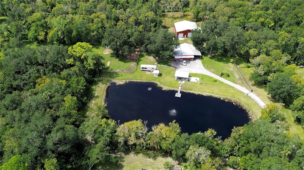 An aerial view shows a pond, a house, a barn, and an RV on wooded land — 2310 DOSTER DRIVE, NEW SMYRNA BEACH, FL