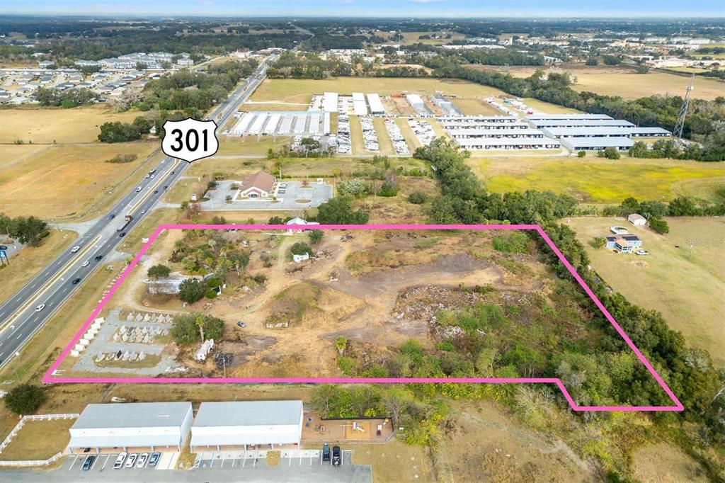 An aerial view shows a vacant, partially cleared lot outlined in pink next to a highway — 10973 N US HIGHWAY 301, OXFORD, FL