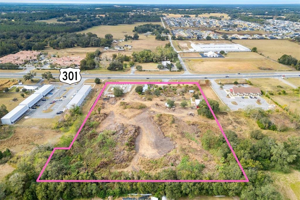 An aerial view shows a vacant, partially cleared lot outlined in pink along a highway — 10973 N US HIGHWAY 301, OXFORD, FL