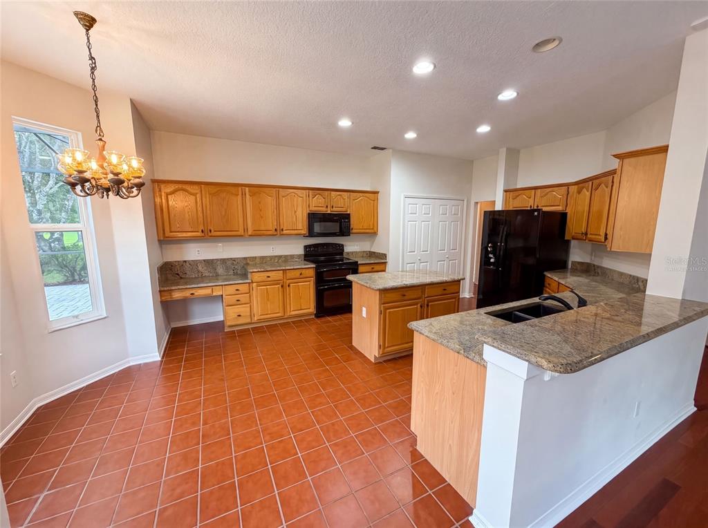 A kitchen features oak cabinets, granite countertops, a center island, and terracotta tile flooring — 1379 HAMPSTEAD TERRACE, OVIEDO, FL
