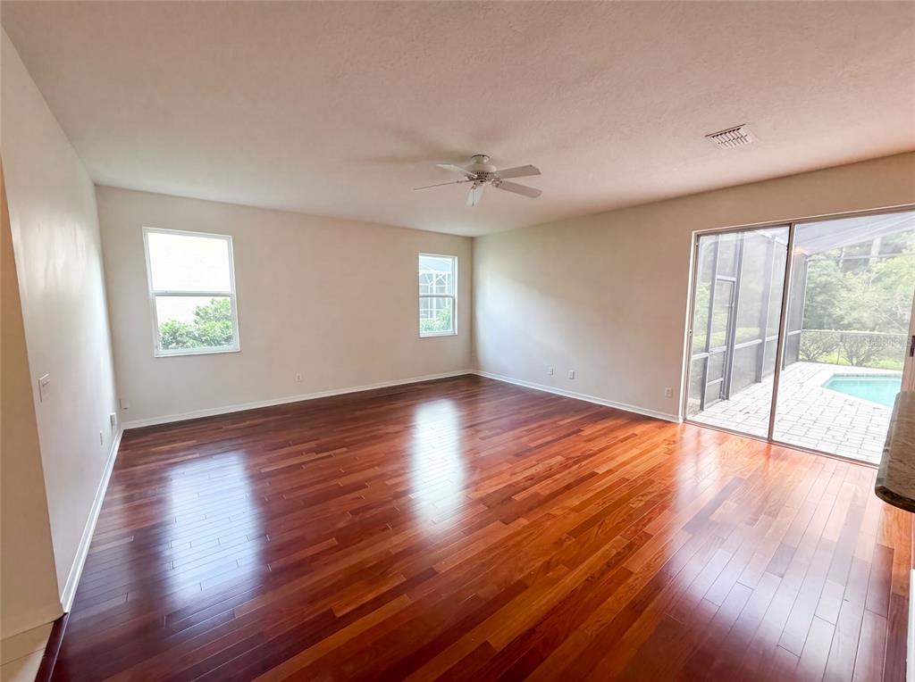 An empty living room features hardwood floors, a ceiling fan, and sliding glass doors to a pool — 1379 HAMPSTEAD TERRACE, OVIEDO, FL