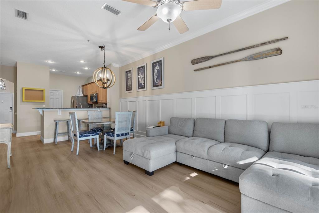 A living room with a gray sectional sofa, wainscoting, and a dining area with chairs — 15 OCEAN CREST WAY UNIT 1314, PALM COAST, FL