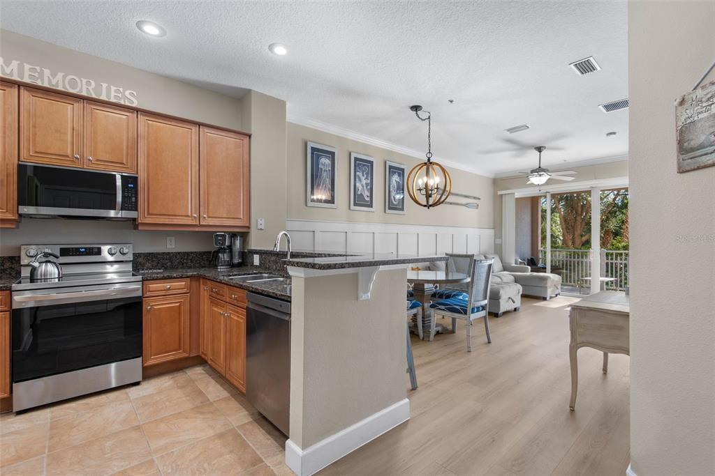A kitchen with wood cabinets and granite countertops opens to a dining area and balcony — 15 OCEAN CREST WAY UNIT 1314, PALM COAST, FL