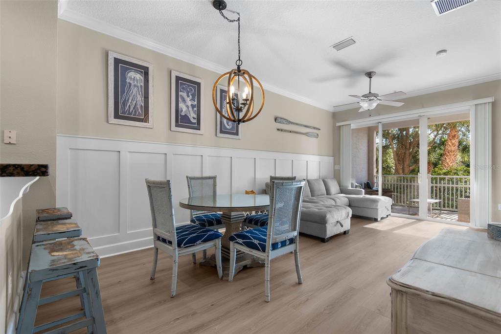 A dining area and living room with light wood floors, wainscoting, and a glass-topped table — 15 OCEAN CREST WAY UNIT 1314, PALM COAST, FL
