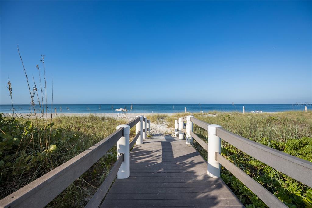 A wooden boardwalk with railings leads through sand dunes toward the ocean beach — 1095 GULF OF MEXICO DRIVE UNIT 102, LONGBOAT KEY, FL