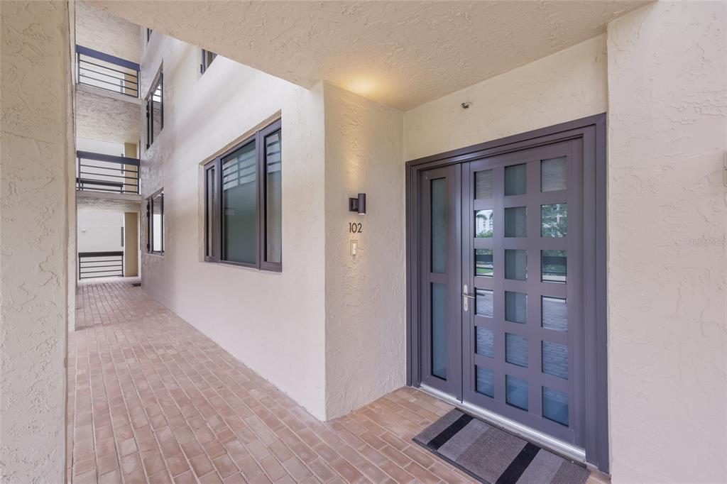A ground-level apartment entrance features a dark gray double door and a brick walkway — 1095 GULF OF MEXICO DRIVE UNIT 102, LONGBOAT KEY, FL