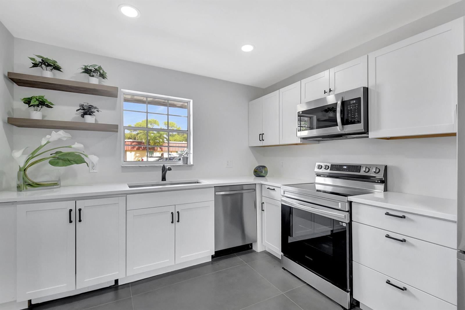 A modern kitchen features white cabinets, stainless steel appliances, gray tile floors, and open shelving — 868 Worcester Lane # B, Lake Worth FL 33467, LAKE WORTH, FL