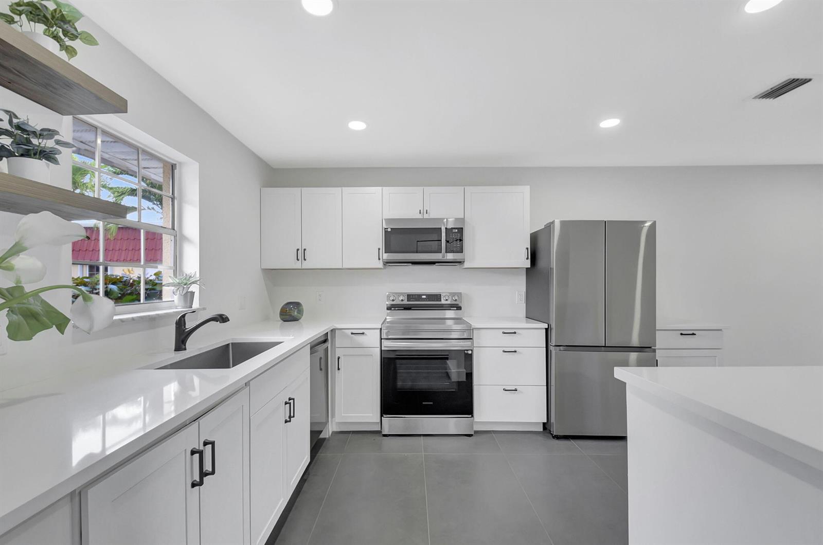 A modern kitchen features white cabinets, stainless steel appliances, quartz countertops, and gray tile flooring — 868 Worcester Lane # B, Lake Worth FL 33467, LAKE WORTH, FL