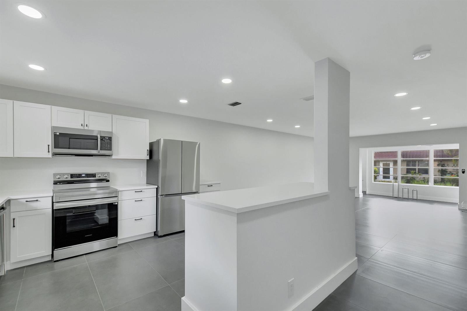 A modern kitchen features white cabinets, stainless steel appliances, and gray tile flooring — 868 Worcester Lane # B, Lake Worth FL 33467, LAKE WORTH, FL