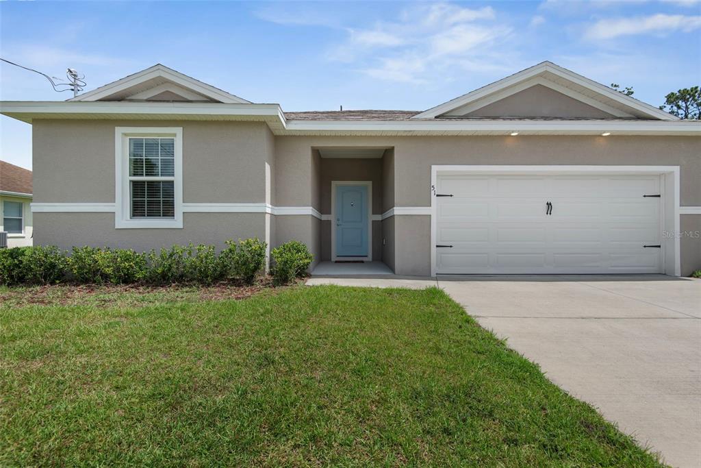 A single-story house with a beige stucco exterior, a white garage door, and a blue door — 51 ROYAL OAK DRIVE, PALM COAST, FL