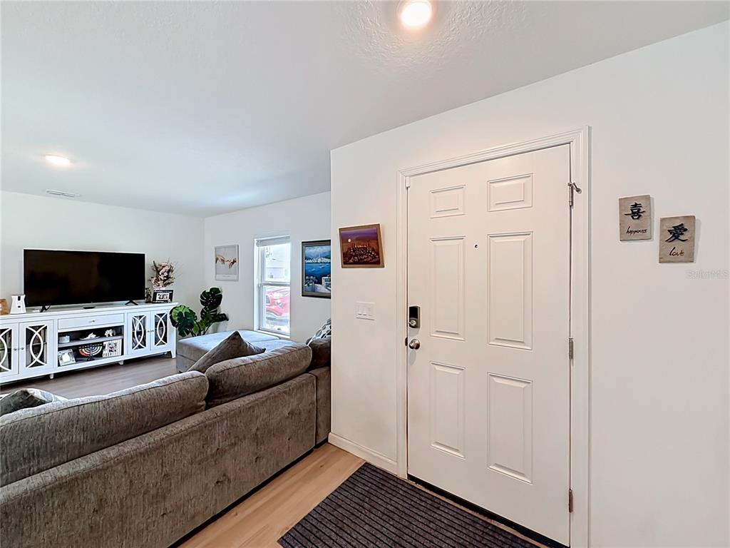 A living room with a gray sofa, white media console, and a white front door — 3159 ASPEN ROAD, PALM BAY, FL