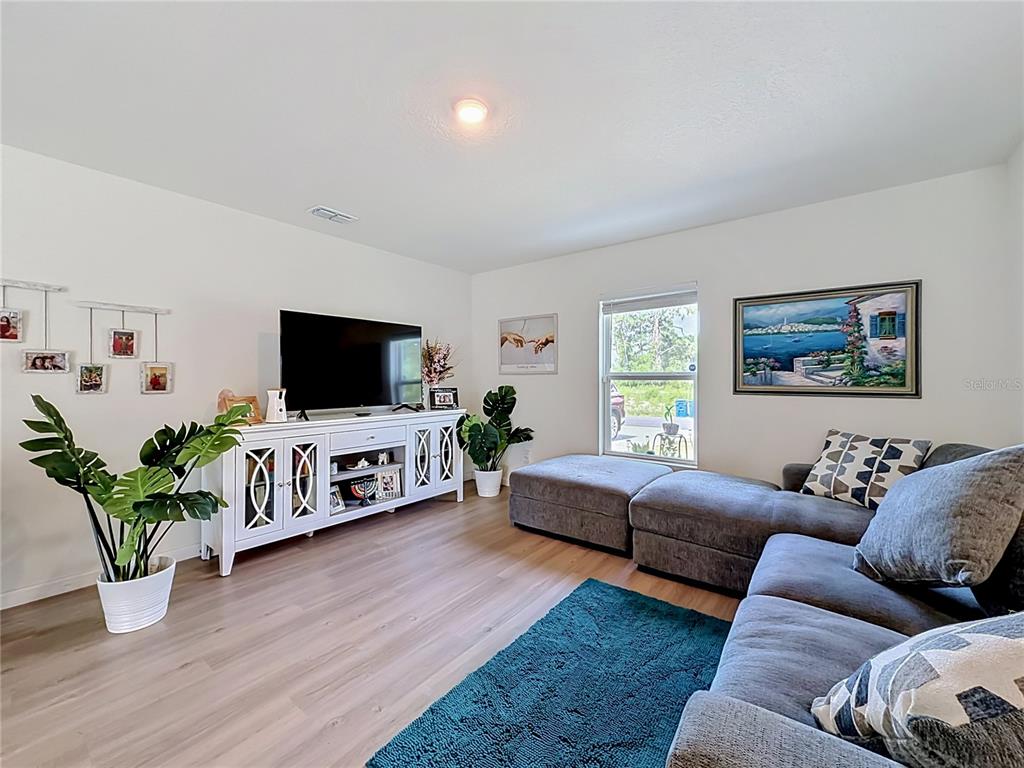 A living room features a grey sectional sofa, a white media console, and light flooring — 3159 ASPEN ROAD, PALM BAY, FL
