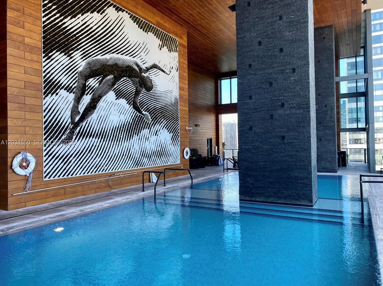 An indoor swimming pool features a large black and white mural on a wood-paneled wall — MIAMI, FL