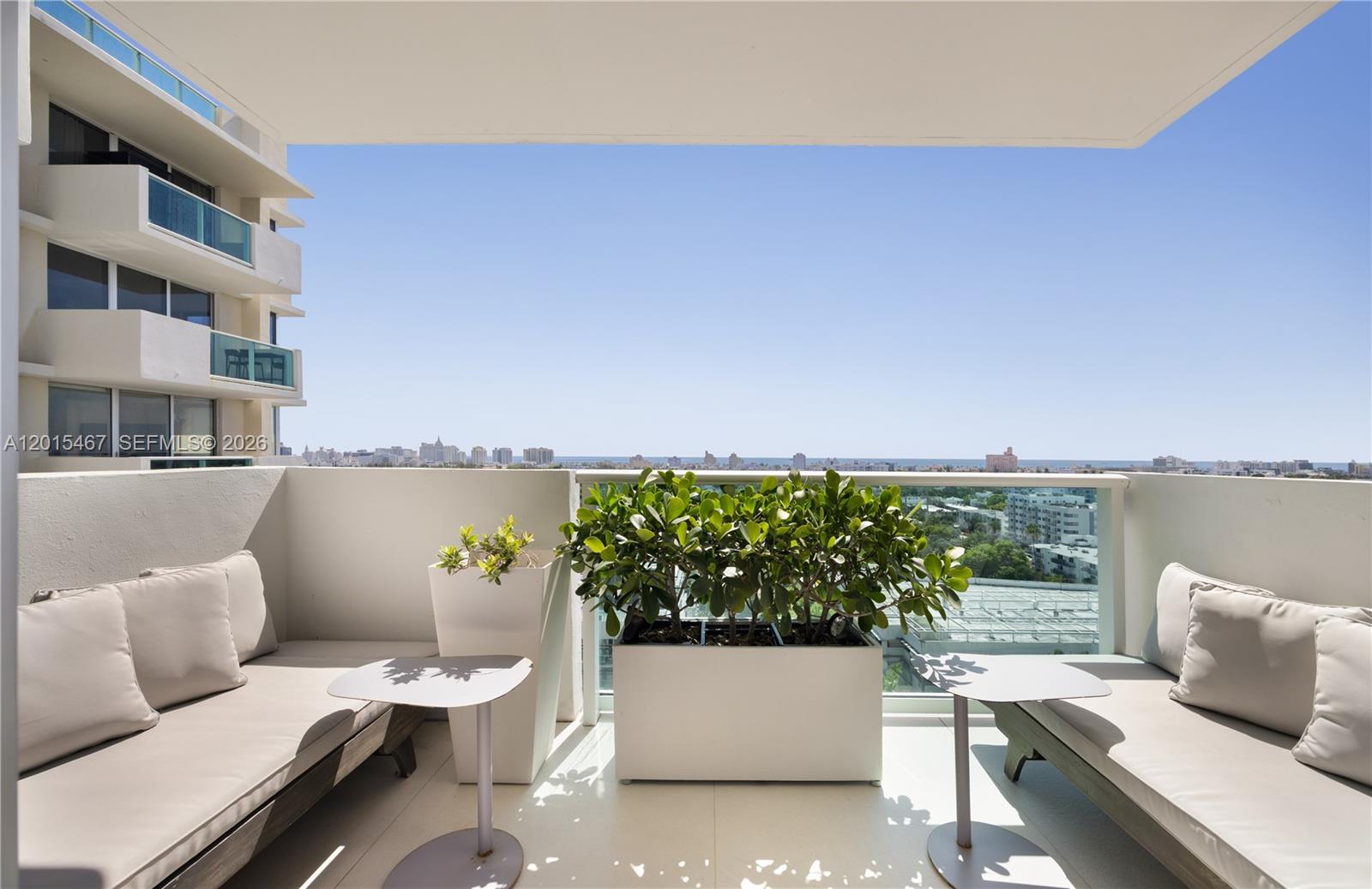 A balcony features two lounge chairs, small tables, and a large planter against a glass railing — 1200 West Ave # 1410, Miami Beach FL 33139, MIAMI BEACH, FL