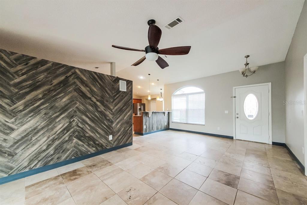 An open living area features a herringbone wood-paneled wall, tile flooring, and a ceiling fan — 637 REGENCY WAY, KISSIMMEE, FL
