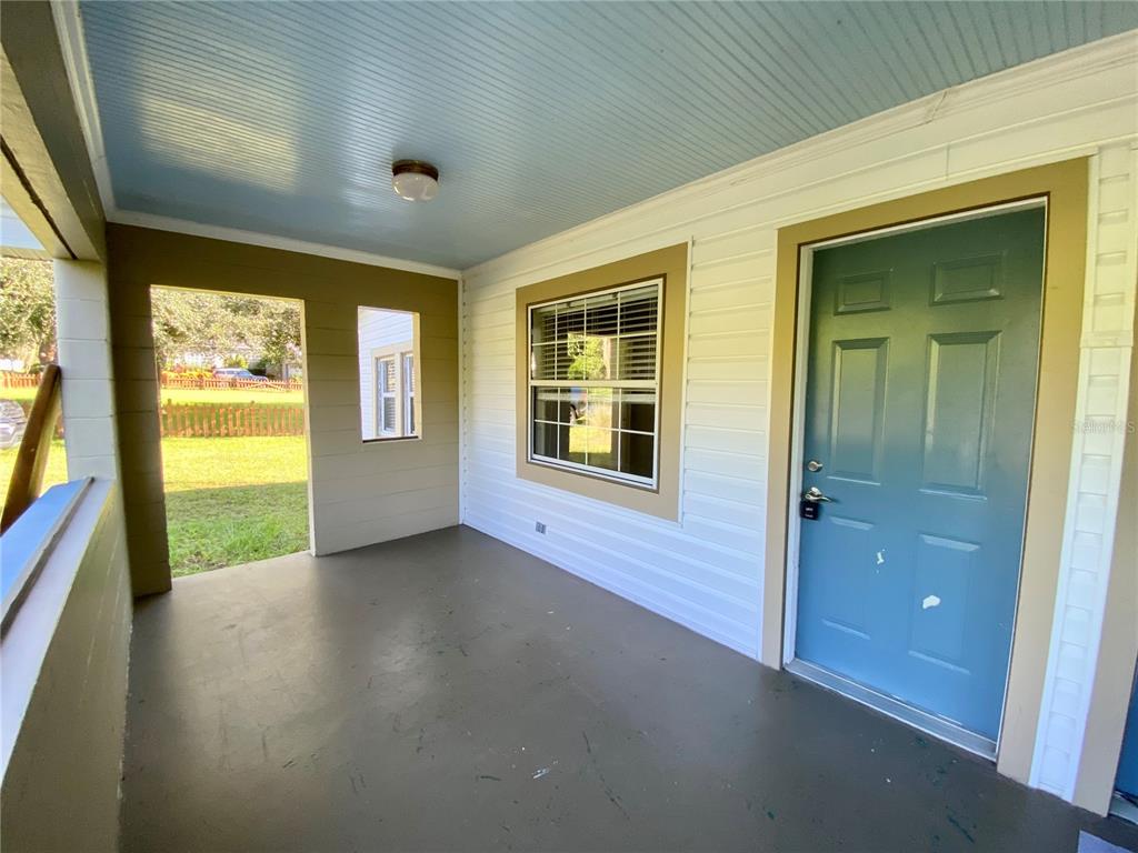 A covered porch features a blue door, a window with blinds, and a painted floor — 13650 5TH STREET, DADE CITY, FL