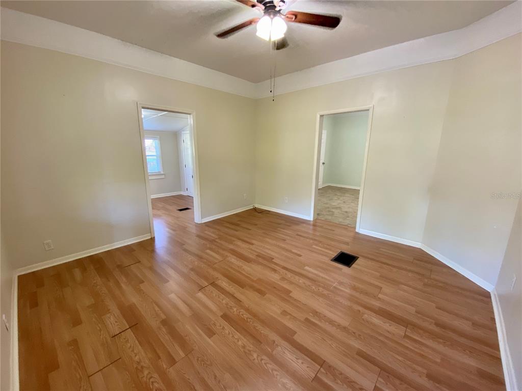 An empty room features light-colored walls, wood-look laminate flooring, a ceiling fan, and two doorways — 13650 5TH STREET, DADE CITY, FL
