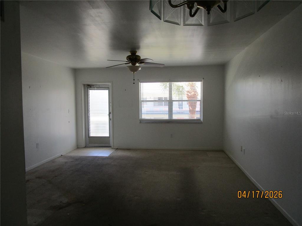 An empty living room features beige carpeting, a ceiling fan, and a sliding glass door — 5900 21ST STREET N UNIT 15, ST PETERSBURG, FL
