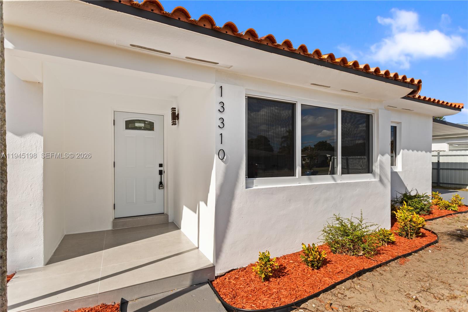 The exterior of a white house features a tiled roof, a front door, and windows — 13310 NW 17th Pl, Miami FL 33167, MIAMI, FL