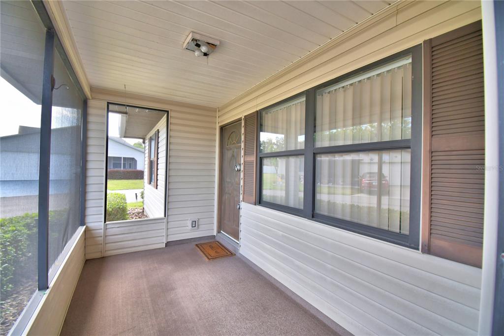 A covered porch with light-colored siding, a brown front door, and a screened-in wall — 4828 SQUIRE HOLLOW DRIVE, LAKELAND, FL