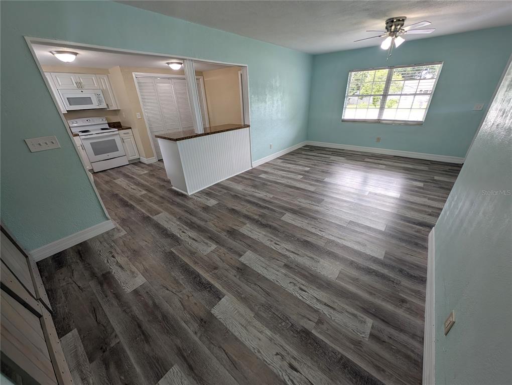 A living room with light blue walls and wood-look flooring opens into a kitchen area — 111 W GRAPEFRUIT CIRCLE, CLEARWATER, FL