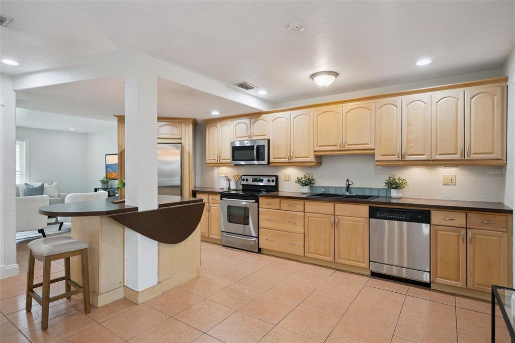 A kitchen features light wood cabinets, stainless steel appliances, dark countertops, and a breakfast bar — 1713 GULFVIEW DRIVE UNIT 435B, MAITLAND, FL