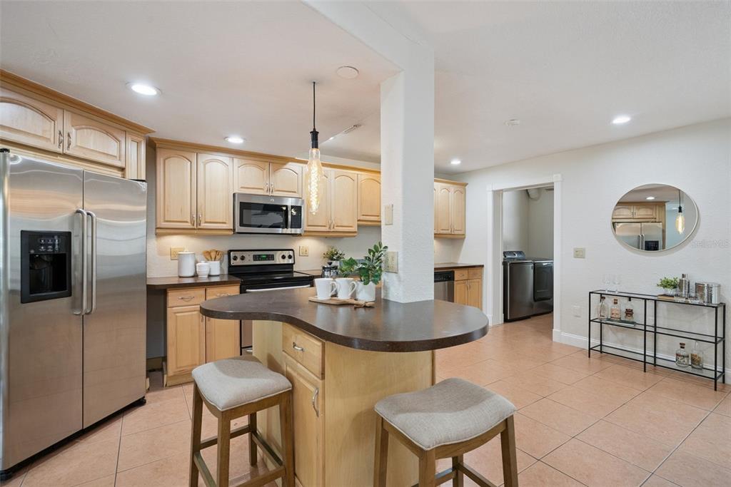 A kitchen features light wood cabinets, stainless steel appliances, a curved island, and tiled flooring — 1713 GULFVIEW DRIVE UNIT 435B, MAITLAND, FL