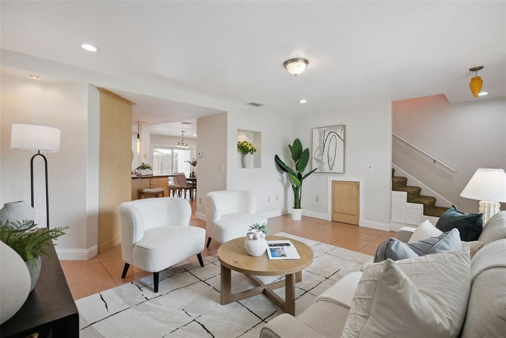 A bright living room features white armchairs, a round coffee table, and stairs leading upward — 1713 GULFVIEW DRIVE UNIT 435B, MAITLAND, FL