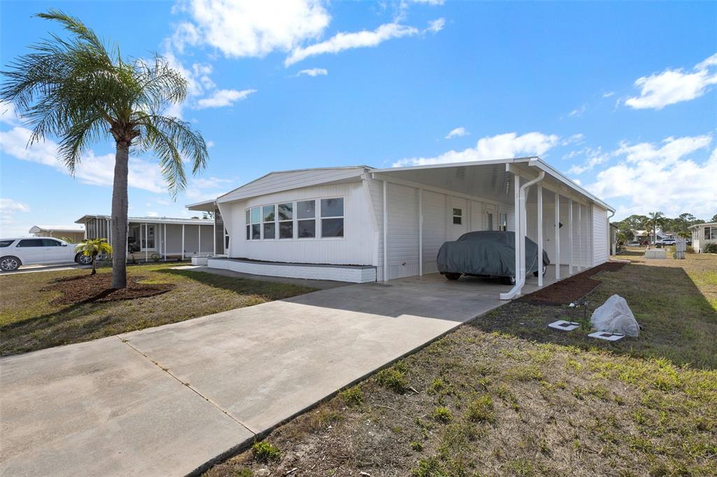 A white mobile home features a carport, a concrete driveway, and a palm tree — 517 LOS ALTOS, NORTH PORT, FL