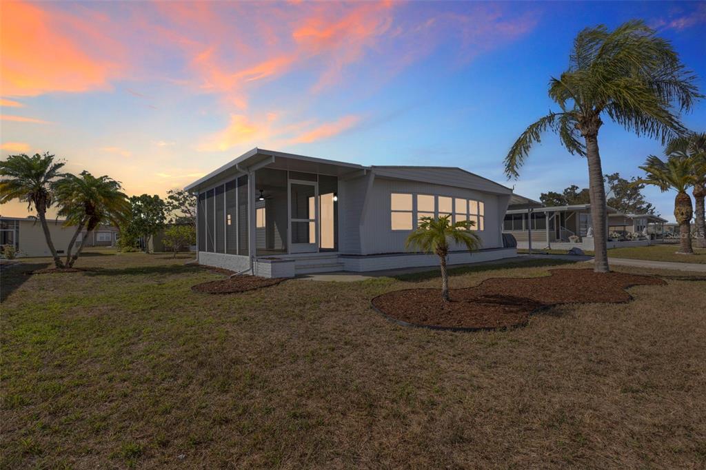 A white mobile home with a screened-in porch sits on a grassy lot at sunset — 517 LOS ALTOS, NORTH PORT, FL