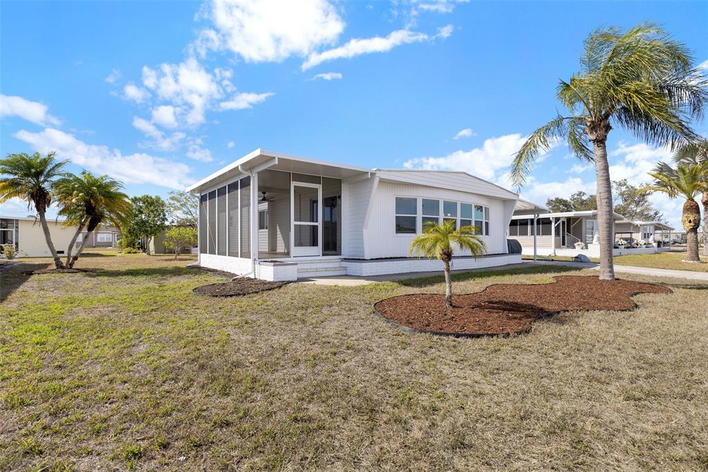 A white manufactured home features a screened-in porch and a small palm tree in front — 517 LOS ALTOS, NORTH PORT, FL